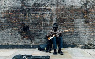 чернокожий музыкант играет на гитаре сидя возле кирпичной стены
