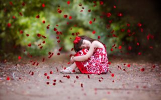 девочка сидит на дорожке под падающими красными лепестками