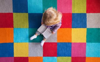 ребенок смотрит книгу на ярком, разноцветном ковре