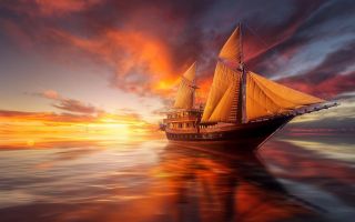 парусник, корабль плывет на фоне красивого заката солнца