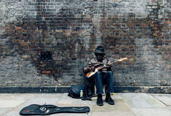 Картинка чернокожий музыкант играет на гитаре сидя возле кирпичной стены