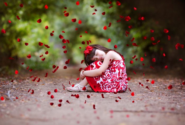 Картинка девочка сидит на дорожке под падающими красными лепестками