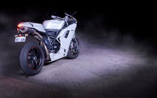 красивый белый мотоцикл Ducati 1198 стоит в темноте при свете фар