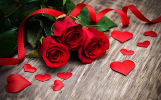 три красные розы с лентой возле сердечек на полу