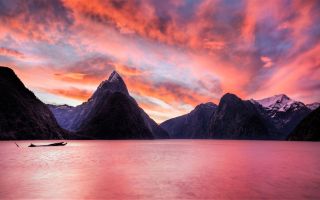 озеро на фоне острых гор на закате солнца и огненного неба